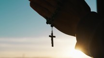 Silhouette of Hand of Man praying at sunset with rosary