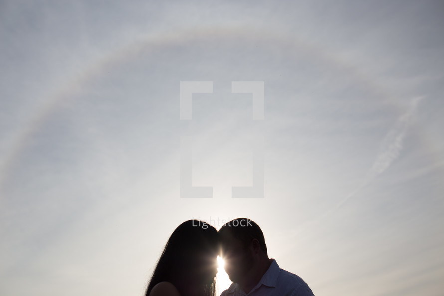 silhouette of a couple forehead to forehead and a sunburst 