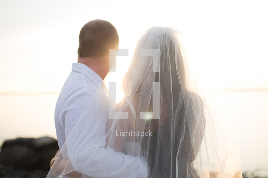 A bride and groom stand together looking at the sun.