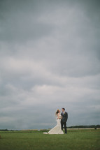 Bride and groom - field - cloudy sky