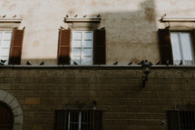Pigeons sitting on the windowsills and ledge of a stone building.