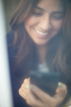 a smiling woman looking at a cellphone screen 