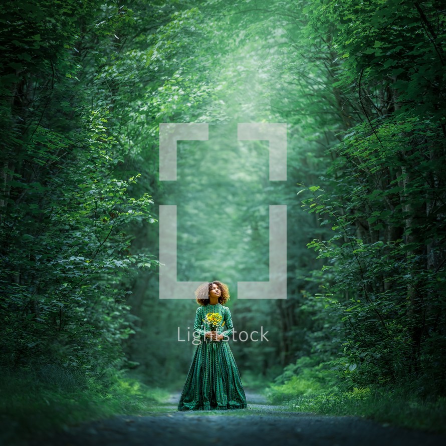 a girl in a green dress standing outdoors in a forest 