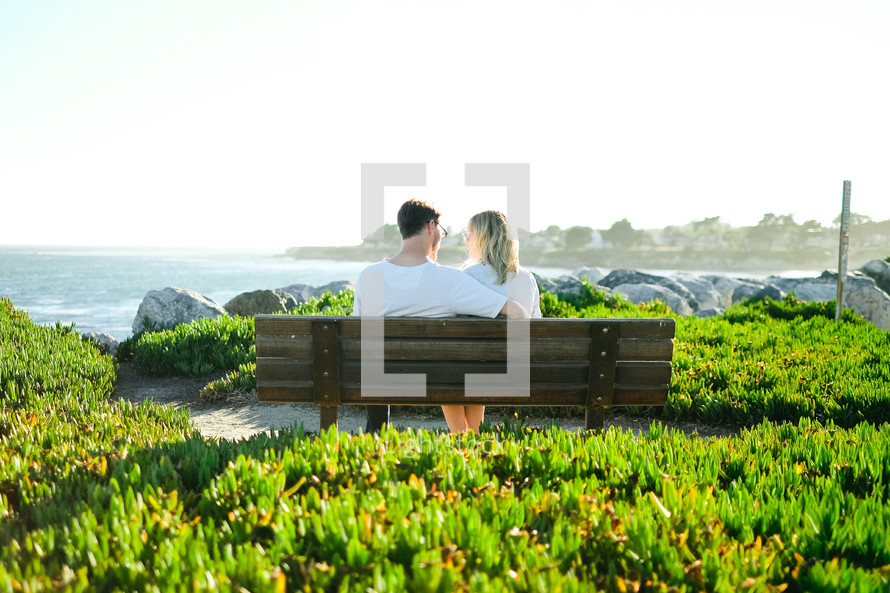 couple sitting on a park bench near the ocean 