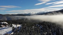 aerial view over low hanging clouds over a snow covered landscape 