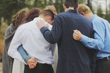 a group of young adults praying in circle