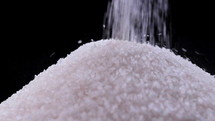 Pouring white sugar on black background in slow motion. The benefits or the danger of sugar consumption to health concept.