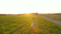 Two happy young girls running together in a green field during sunset
