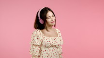 Attractive woman dancing listening to music, dancing with headphones on pink studio background. Radio, happiness, freedom, youth concept
