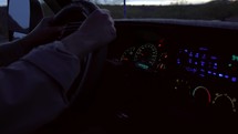A mans hands on steering wheel while driving at dusk