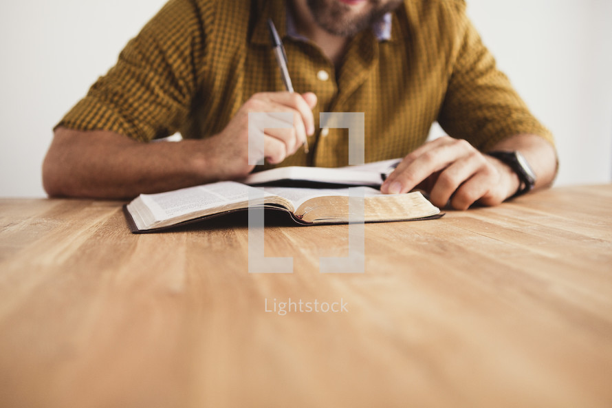 man reading a Bible and writing in a journal