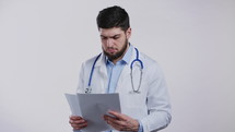 Satisfied man in professional medical coat holding files papers isolated on white background. He nods his head approvingly to diagnosis. Doc with beard and stethoscope. High quality 4k footage