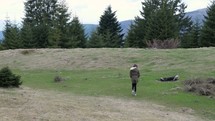 Video of a young girl walking on a green field to the edge of a forest.
