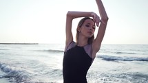 Young girl with long hair practicing classic ballet exercises with emotions. Dancing ballerina in black silk dress on embankment near ocean or sea at sunrise or sunset.