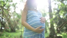 pregnant woman standing outdoors holding her belly 