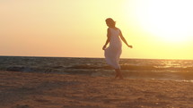 Silhouette of a woman running on the shore of a beach at sunset.