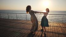 Beautiful girls spinning around wirh hands, dancing and playing on the embankment near sea or ocean. Friendship concept. Sunrise or sunset light. Adult women