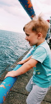toddler boy looking over a railing at water below 