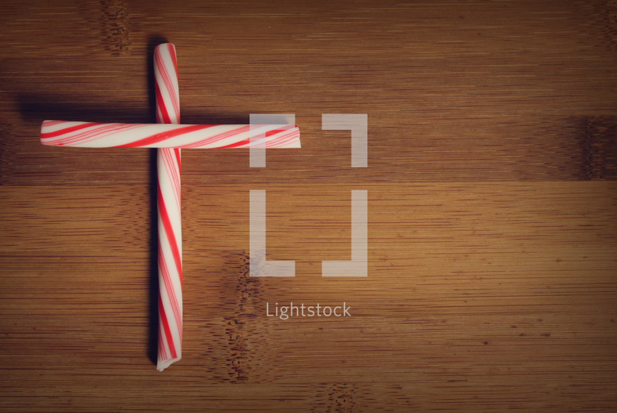 A cross made from peppermint sticks on a wooden table.