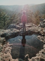 a boy child standing near a puddle on a mountaintop 