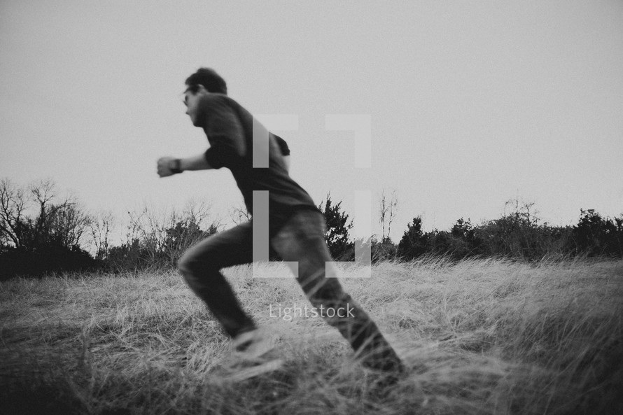 Young man running in a field surrounded by tall grass and trees.