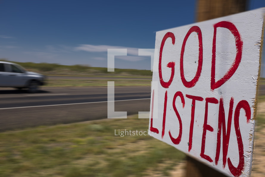 "God Listens" sign nailed to a post on the side of the road.