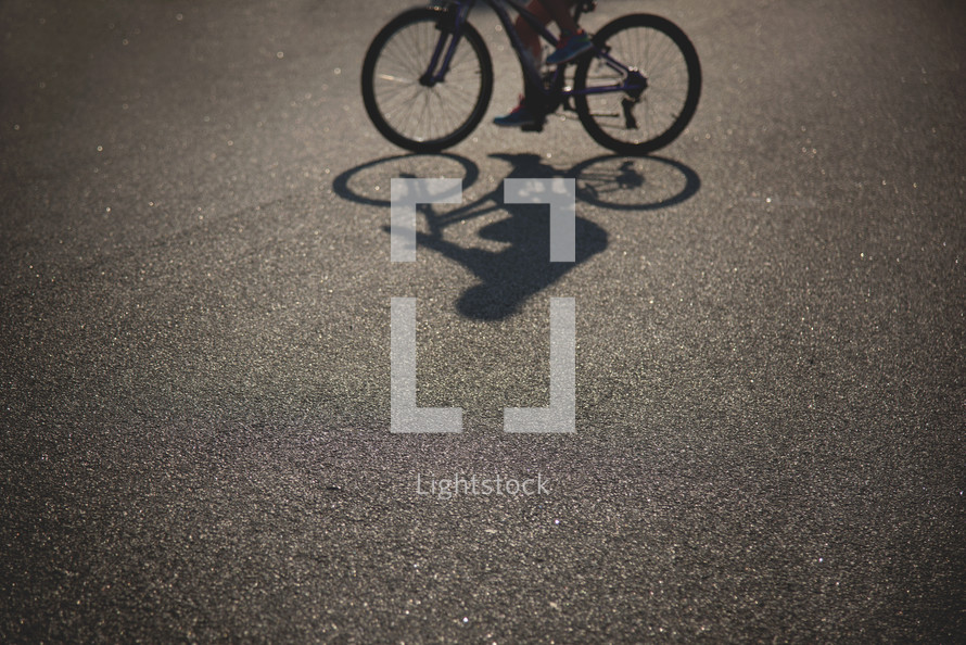 A bicycle and rider and shadow on pavement.