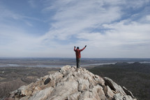 man standing on top of a mountain with his hands raised in worship to God
