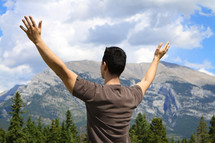 man with his hands raised in worship and praise to God in the mountains