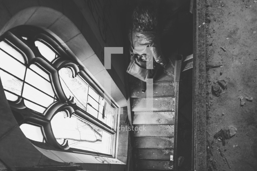 Girl walking up stairs exploring an abandoned church with stained glass window lighting the scene.