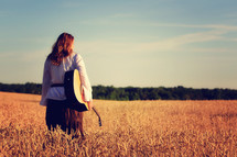 woman standing in a wheat field holding a guitar 