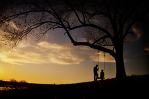 Silhouette of a couple with a tree swing at sunset.