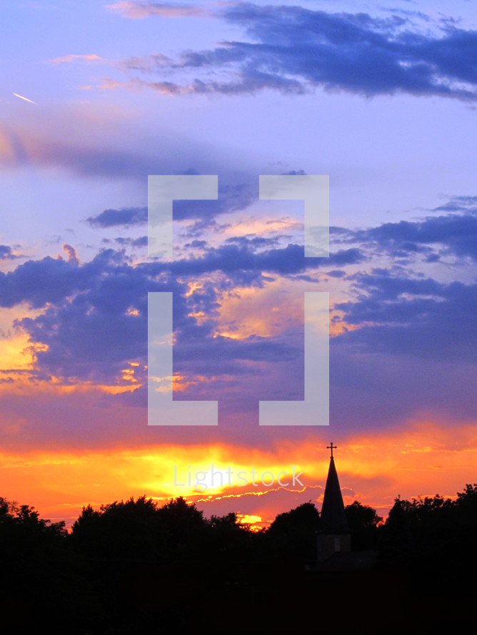 Vivid sunset silhouettes church steeple with cross.