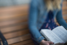 blurry image of a woman on a park bench reading a Bible 