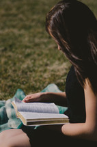woman sitting on a blanket in the grass reading a Bible 