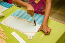 a girl gluing popsicle sticks to paper 