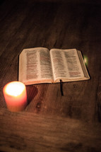 Open BIble and lit candle on wooden table.