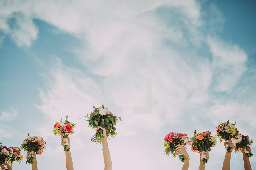 Hands holding flower bouquets toward the sky.