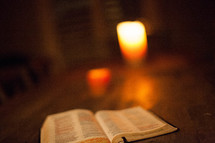 Open Bible and lit candle on wooden table.