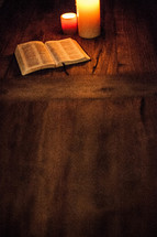 open Bible on a wood table and burning candles