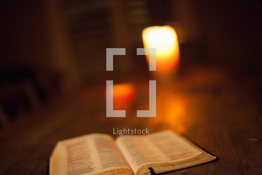 Open Bible and lit candle on wooden table.