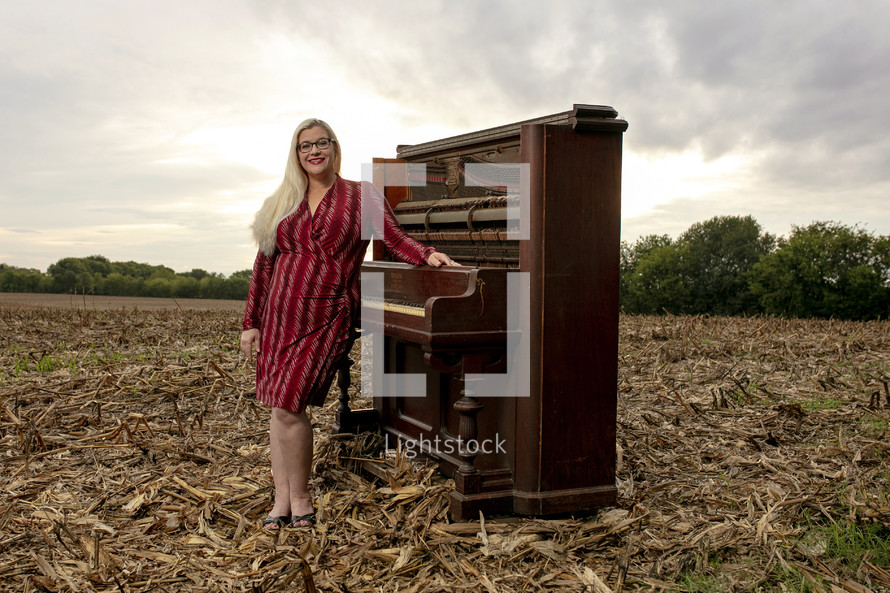 a woman standing next to a piano in a plowed field 