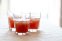 three backlit glasses half filled with watermelon juice and ice