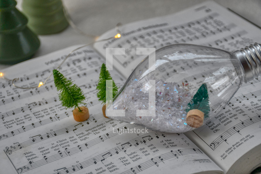 snow in bulb ornament and miniature Christmas trees on a hymnal for Christmas worship service music 