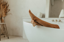 Woman's feet hanging over bathtub in bathroom