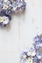Border of purple silk flowers on a white wood background