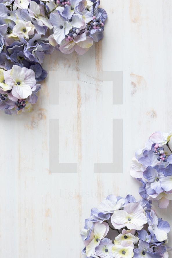 Border of purple silk flowers on a white wood background