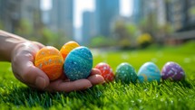 Colorful easter eggs in hand on green grass with city background