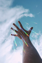 man hand gesturing and reaching in the blue sky with raimbow lights