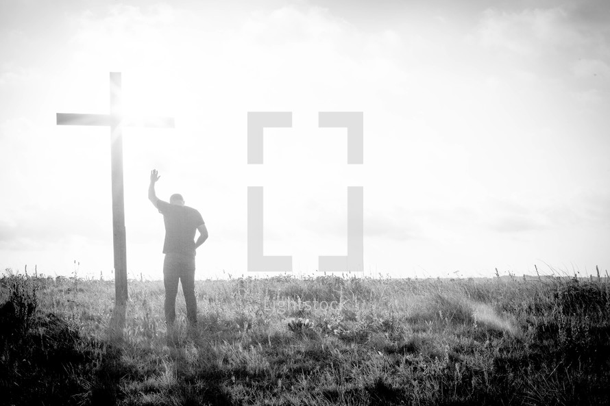 a man praying in front of a cross with raised hand 